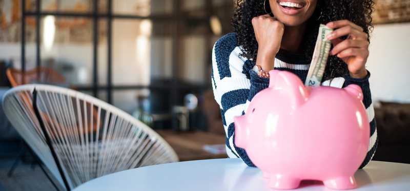 Young adult female putting a dollar bill into a large piggy bank