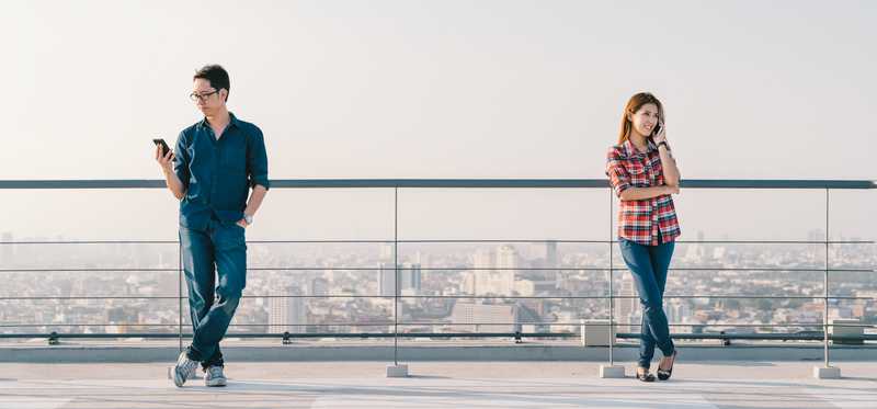 Two young people check their smartphones on a rooftop.