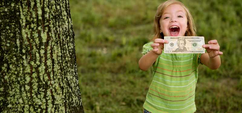 Child standing outdoors excitedly holding a dollar bill.