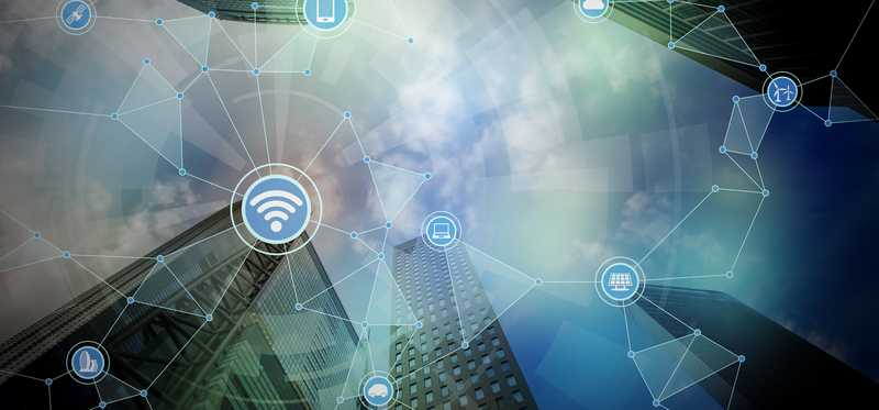 A digital rendering of skyscrapers with internet symbols like WiFi and Bluetooth superimposed over it in a web.