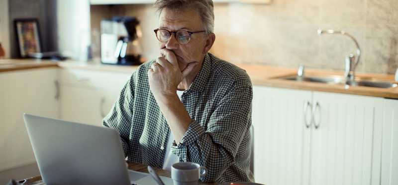 Older man sitting in the kitchen and looking at a laptop