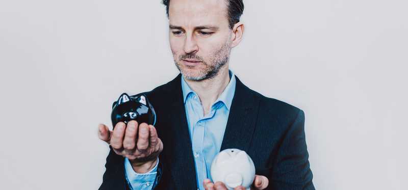 Businessman holding two piggy banks and weighing which to choose
