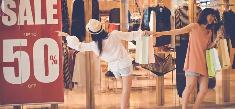 One woman pulling another away from a 50% off sale sign.