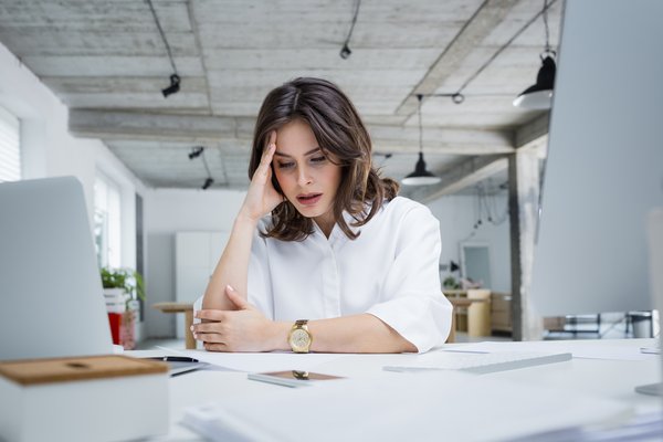 Person with hand on head looks intently at paperwork in office.