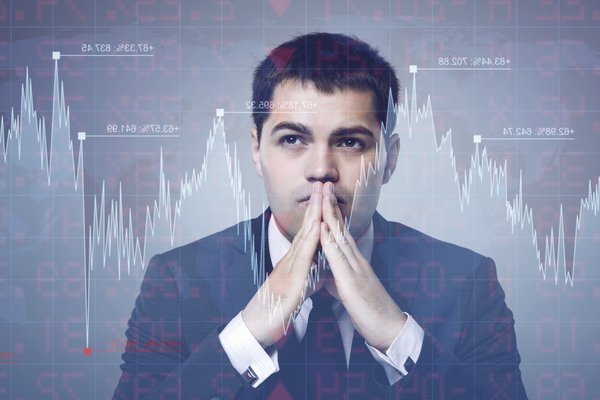 Person with hands in front of face and stock market chart superimposed in the foreground.