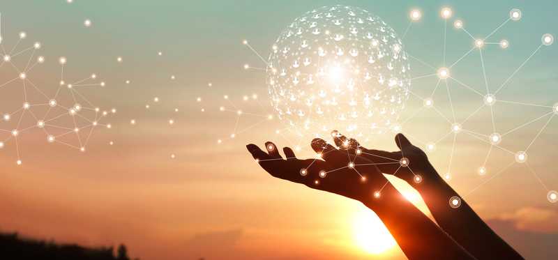 Person holding iridescent sphere in hands against sunset background.