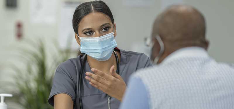 Nurse in mask speaking with patient and holding tablet
