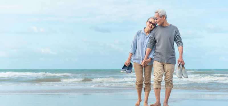 Two people hold hands while walking on the beach.