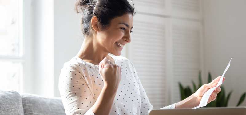 Person with open laptop is looking at paper and smiling.