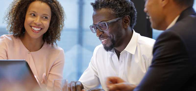 Three smiling people looking at device screen in office.