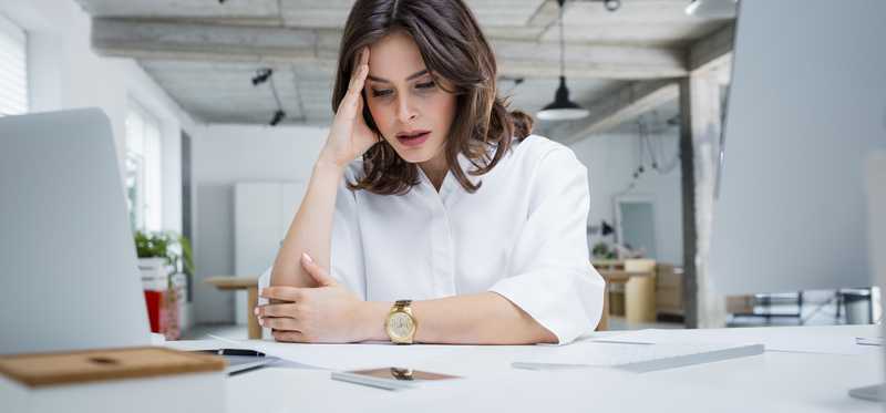 Person with hand on head looks intently at paperwork in office.