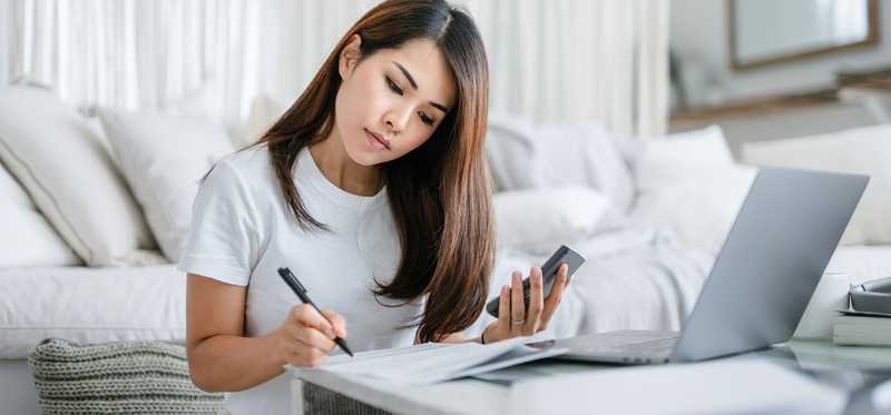 Person taking notes while using phone and laptop.