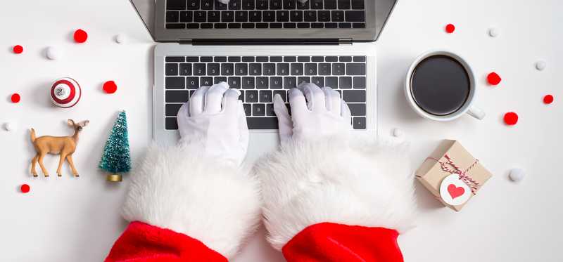 Person dressed in Santa suit with white gloves typing on laptop