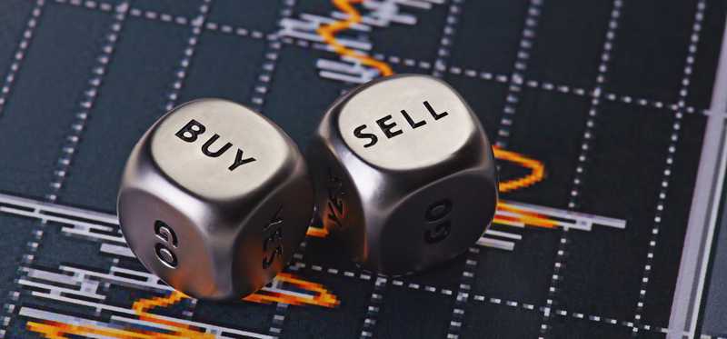 Dice saying Buy and Sell lying on a stock bar chart.