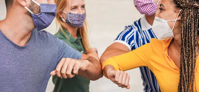 Group of young millennials wearing face masks and elbow bumping