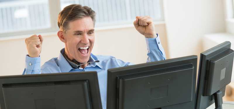 Person raising hands in the air with happiness while looking at three computer screens