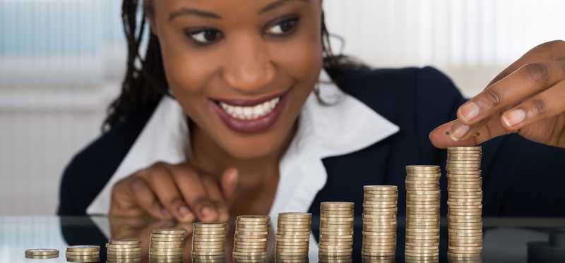 Person smiles behind row of growing stacks of coins.