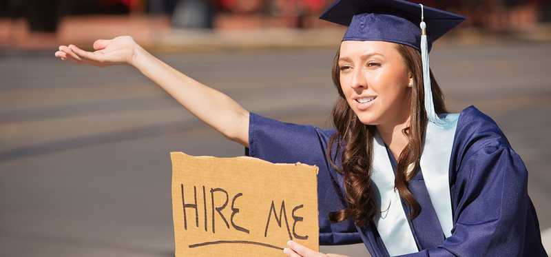 A graduate holding out a sign that reads Hire Me.
