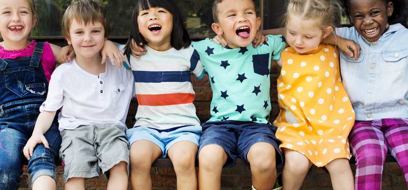 A line of kids sitting together with their arms around each other, laughing