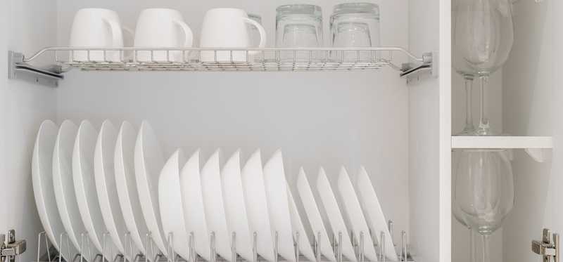 An open white kitchen cabinet containing white dishes and clear glassware.