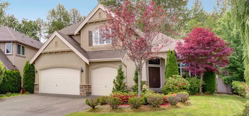 Landscaped home with white garage doors.
