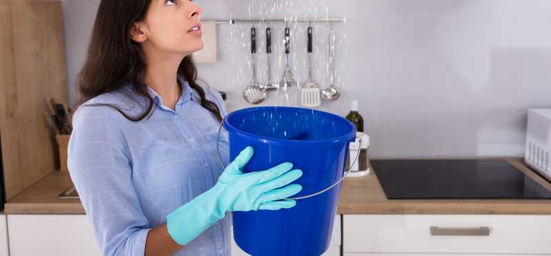 A woman holds a bucket under a leak.