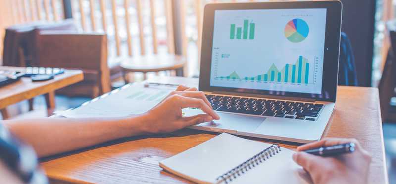 Person taking notes with charts and graphs on laptop screen.