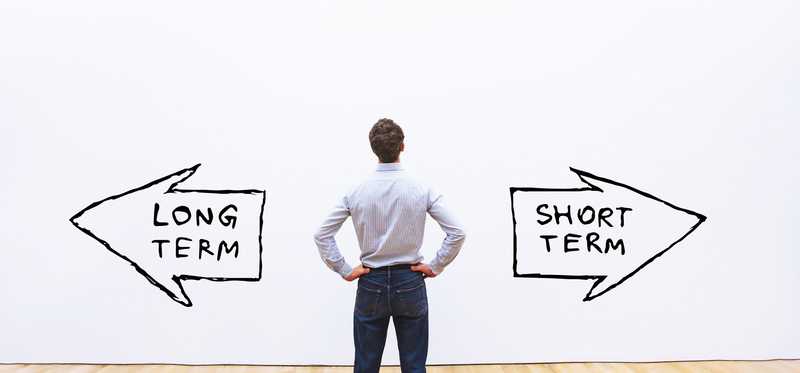 Man stands in front of two arrows, one reading long term and the other reading short term.