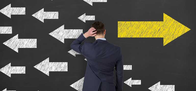 Man stands in front of boards with a bunch of white arrows pointing left and one larger yellow arrow pointing right.