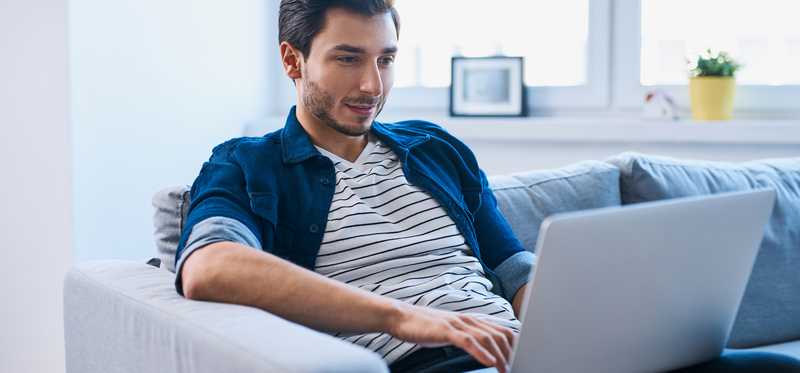 A man sits on a couch with a laptop in front of him.