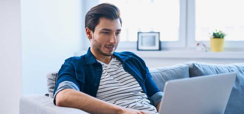A person sitting on a couch while typing on a laptop.