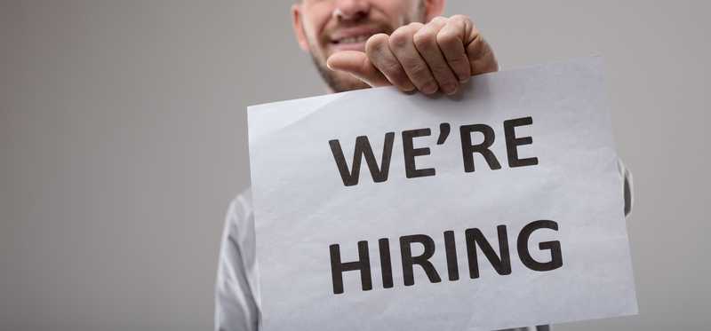 Smiling man holding We're Hiring sign.