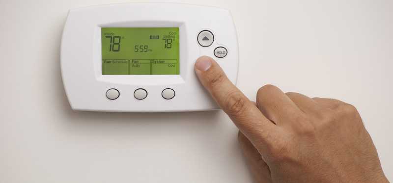 Person pushing button to lower temperature on thermostat.
