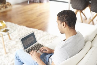 A rear view of a man using a laptop while sitting on a couch.