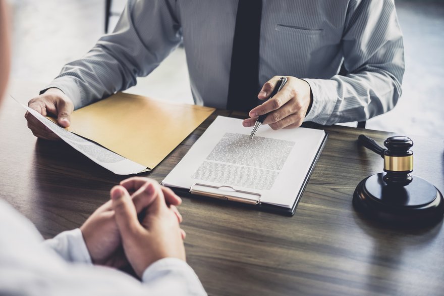 Person with gavel reviewing document across the table from another person.