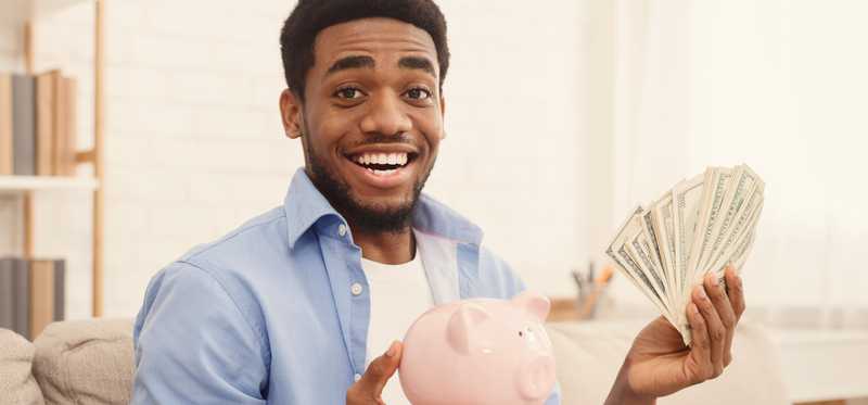 Person smiling while holding cash and a piggy bank.