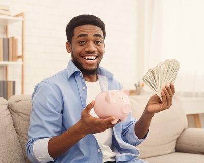 Person smiling while holding cash and a piggy bank.