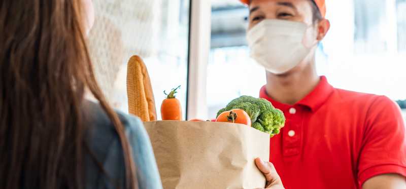 Masked delivery person bringing groceries to a person's home.