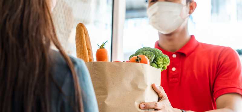 Masked delivery man bringing groceries to a woman's home