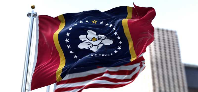 The Mississippi state flag with a tall building in the background.