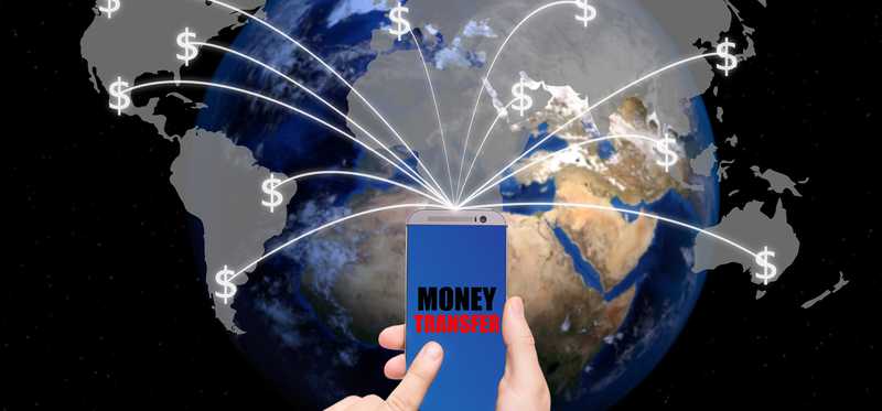 The words "money transfer" on smartphone with lines going from the phone to different parts of the globe
