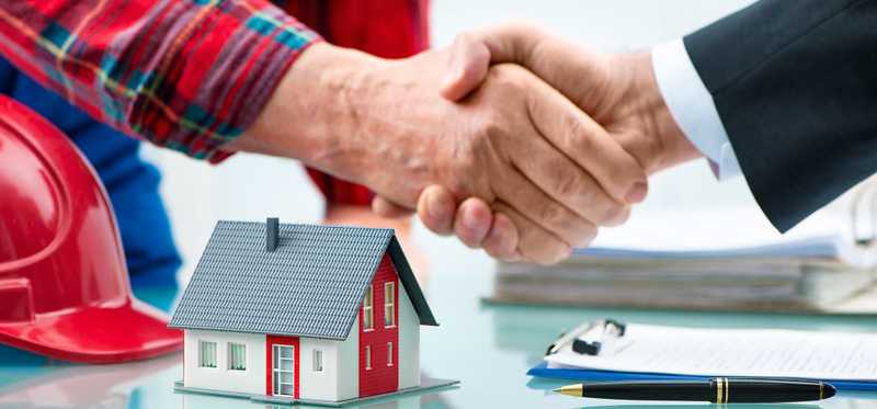 Two people shake hands over the toy model of a house.