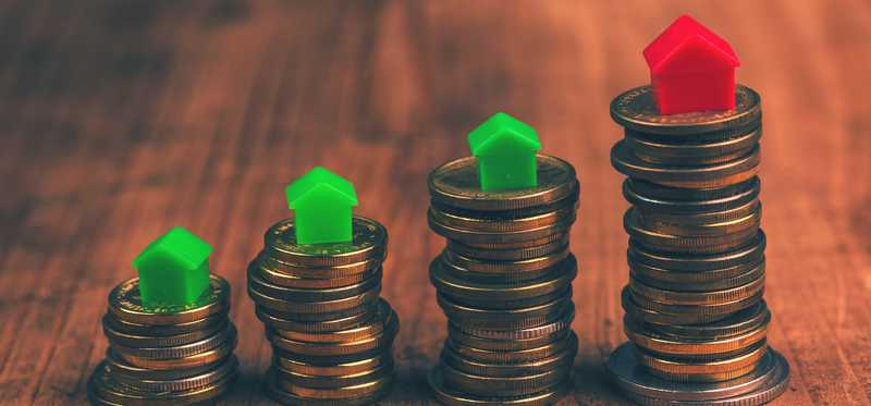 Stacks of coins with red and green Monopoly houses on top rising in height.