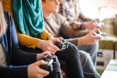 Multiple teenagers seated on a couch while holding video game controllers.