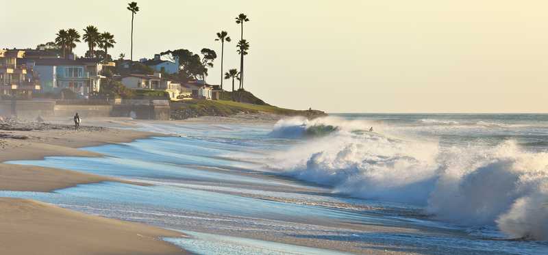 Big waves in San Diego, California, with beach houses in background.