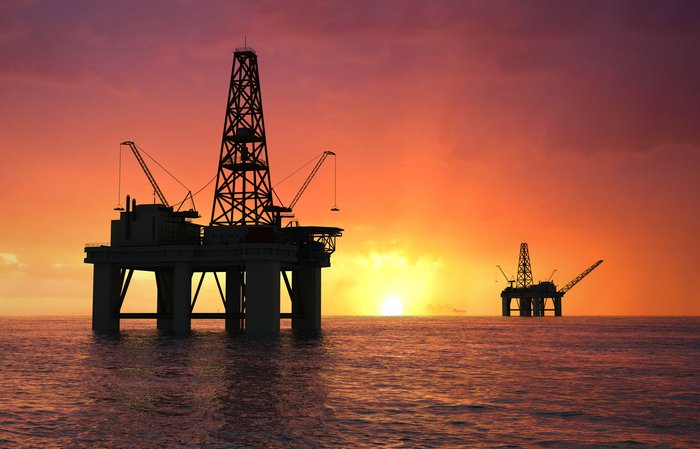 Oil rig silhouette against a reddish golden sunset.
