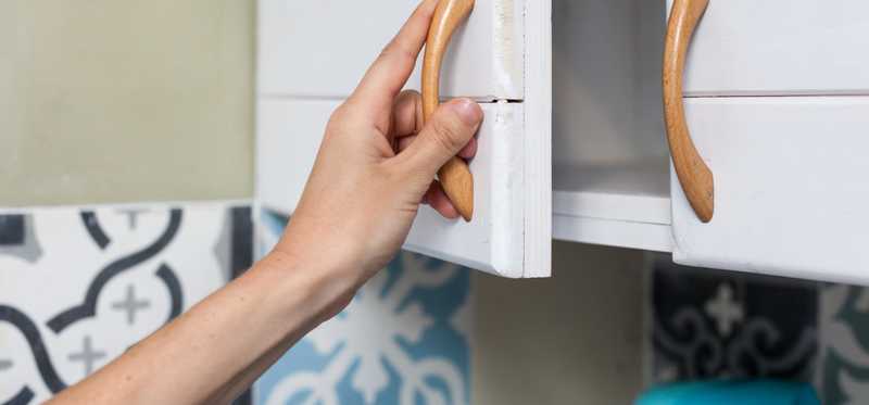 A hand pulling open a kitchen cabinet.