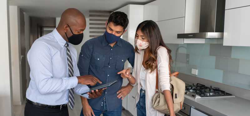 Two people wearing masks while on home tour with masked real estate agent.