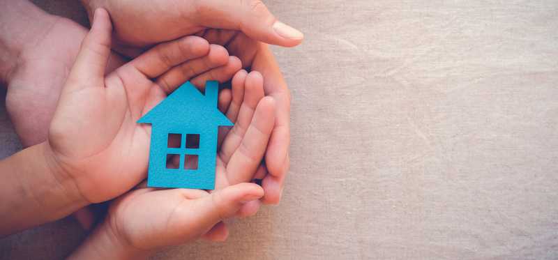 Multiple sets of hands cradle a paper house.