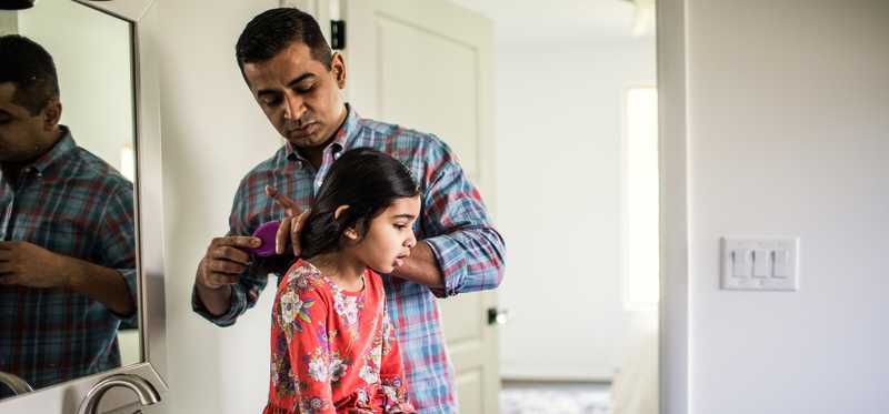 Person brushing child's hair in bathroom.